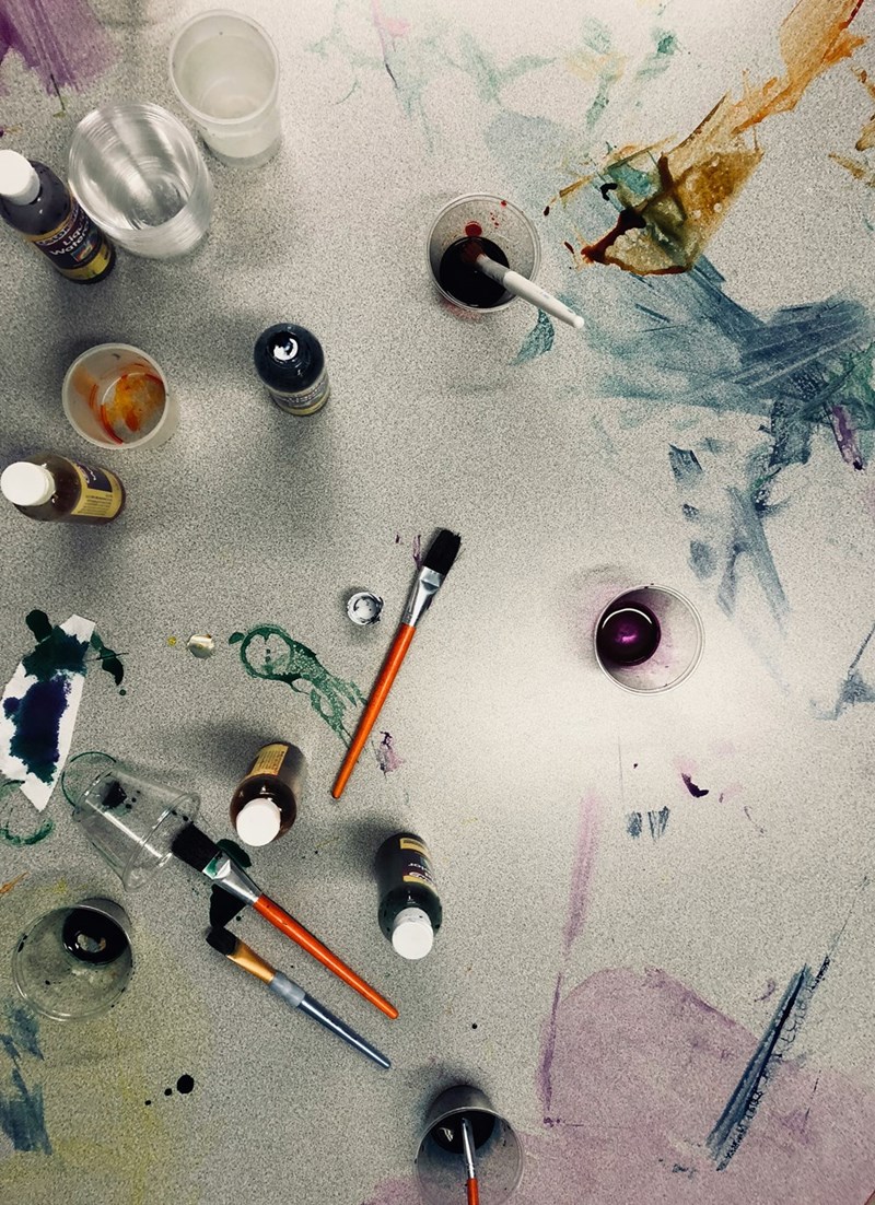 Paint, brushes, and art supplies on a table after a children’s workshop, capturing the creative chaos surrounding the family’s nanny.