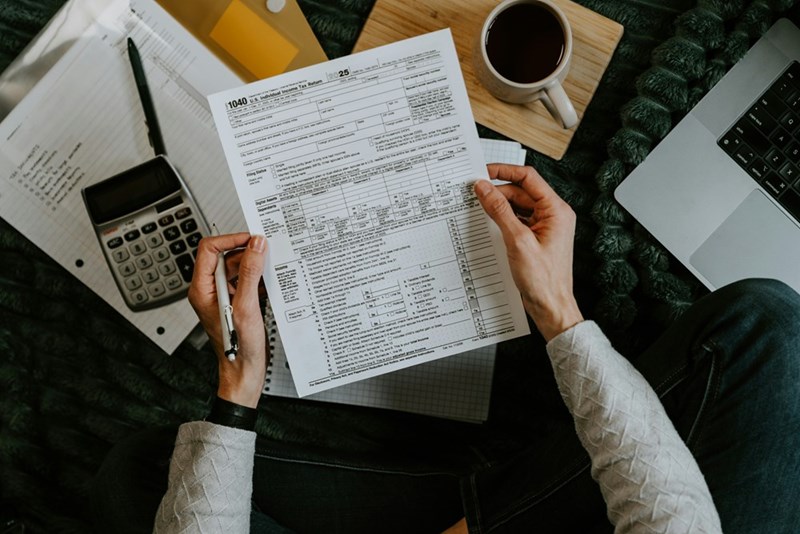 Hands reviewing tax forms beside a calculator and laptop, illustrating the financial pressure behind a disputed $40K Parent PLUS loan.