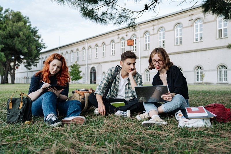 University students studying in the yard of a college campus, illustrating the education expenses that led to a decades-old Parent PLUS loan.