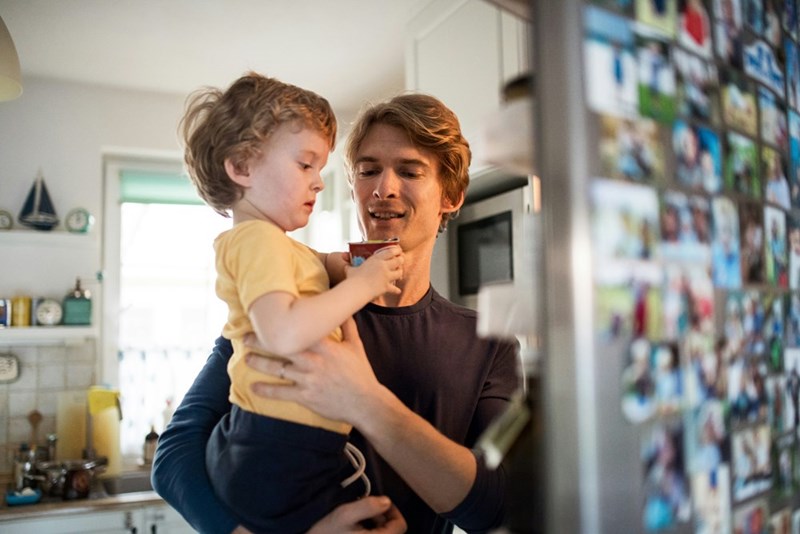 A father carrying his son in his arms, opening the fridge.