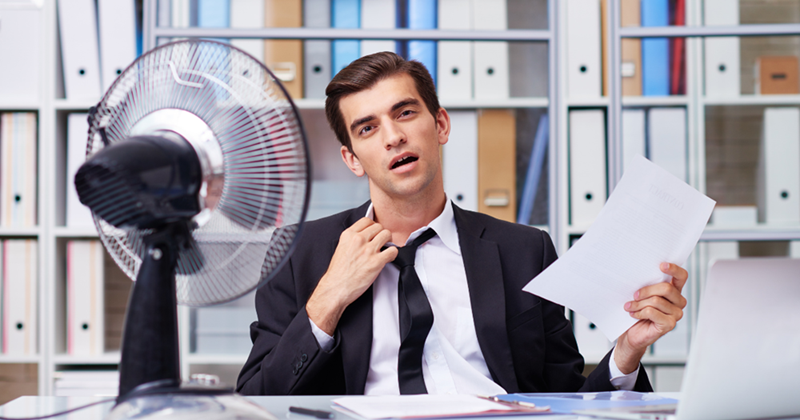 Employee using a desk fan in a hot office.