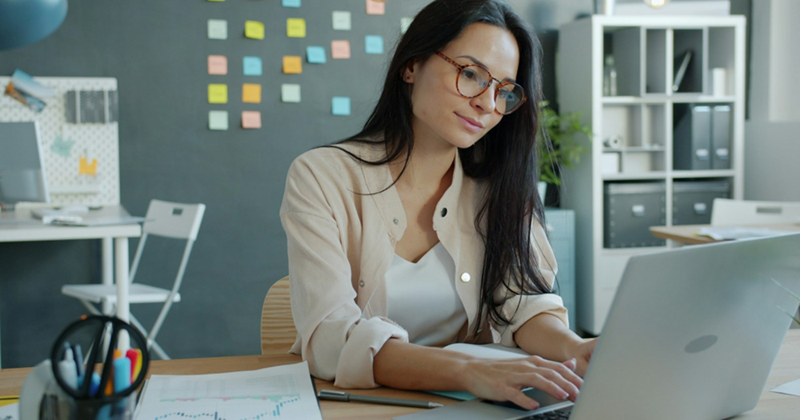 An employee wearing glasses as she works on her laptop in an open-plan office