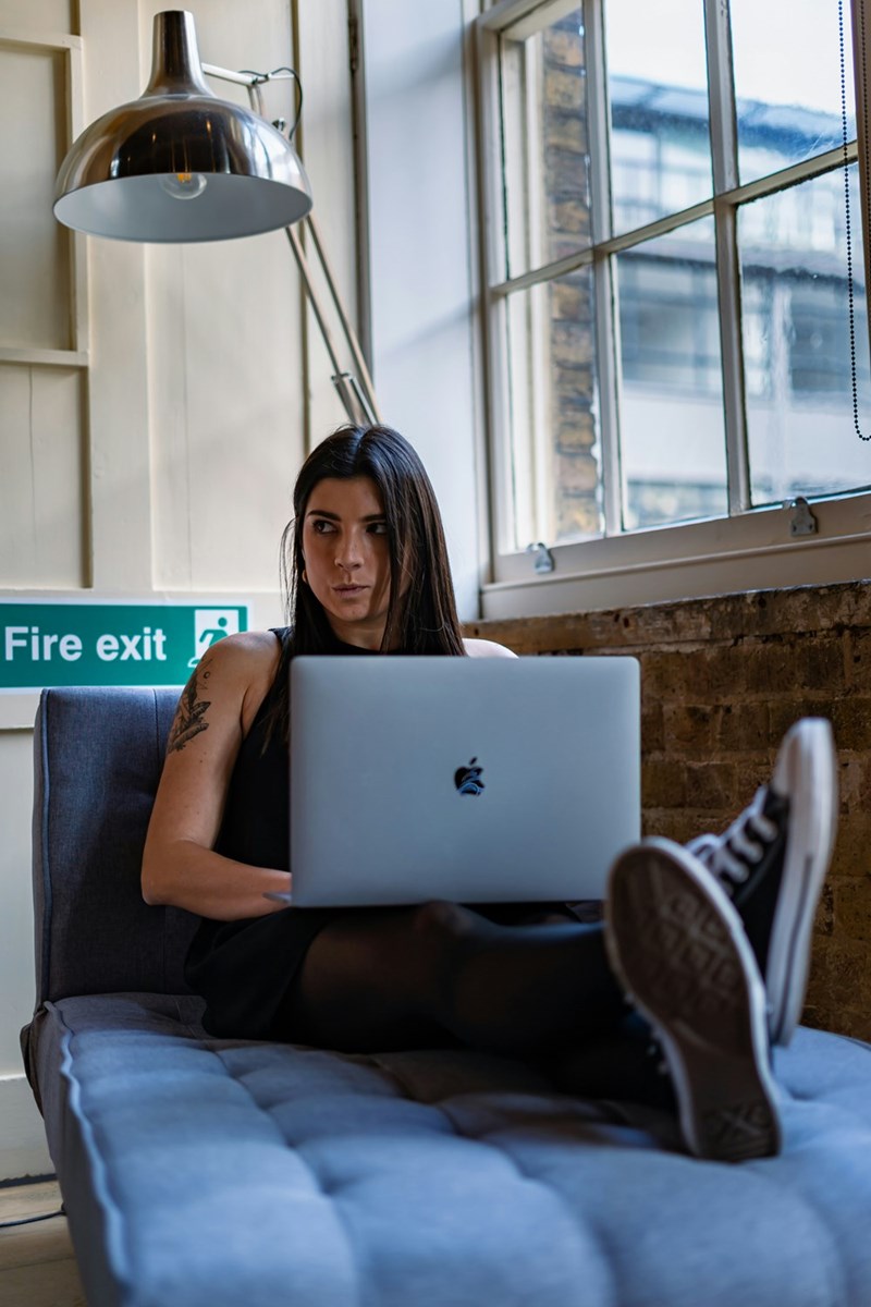Woman sitting behind a laptop with a wary side glance in a windowed room