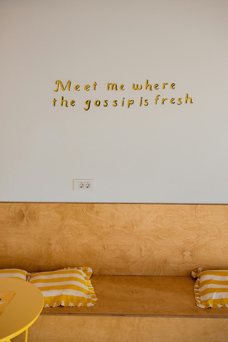 gold lettering on white wall saying 'meet me where the gossip is fresh'