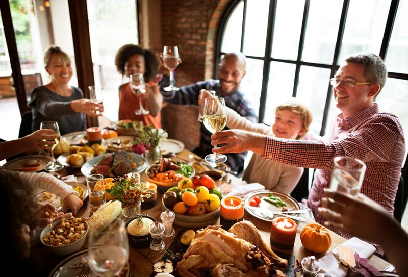 A large family is cheering at a table with glasses and a table full of food.