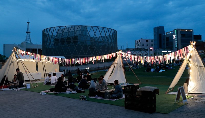 People sitting on green grass during blue hour, surrounded by tents.