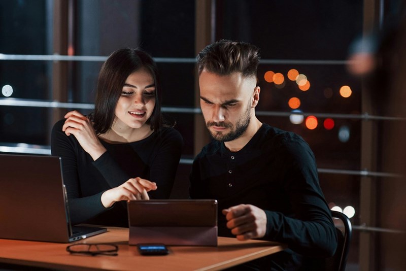 Young couple sitting down looking at a silver computer at night in their living room.