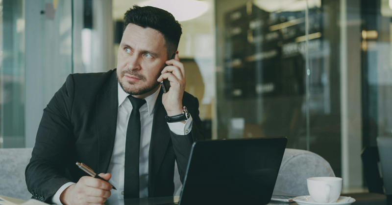 A representation of a man sitting behind a laptop, looking to the side while talking on a cell phone