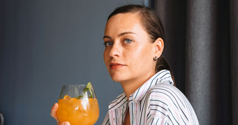 A representation of a woman sitting side-on while holding an orange drink