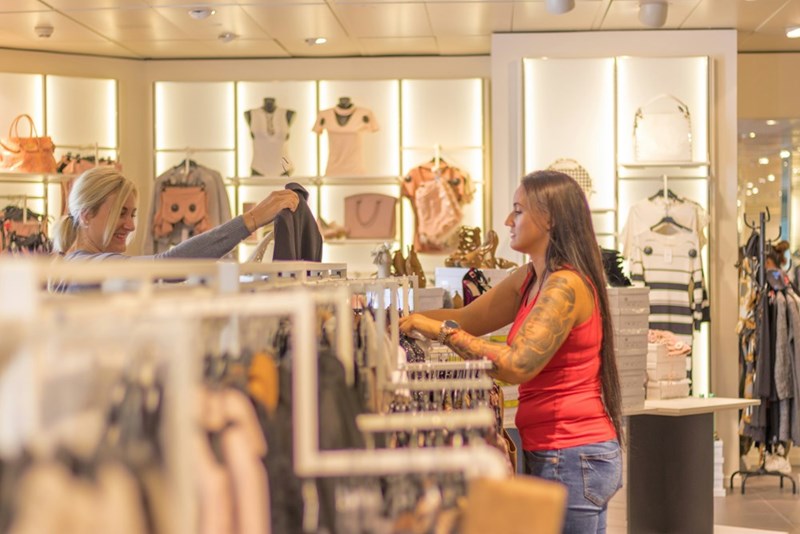 A retail employee in pink tanktop restocks women's clothing in a store