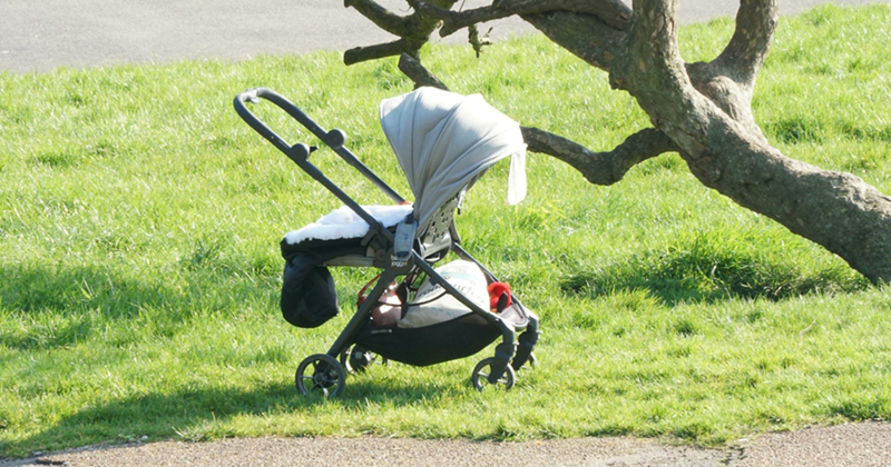 A baby stroller sitting in the grass by a sidewalk
