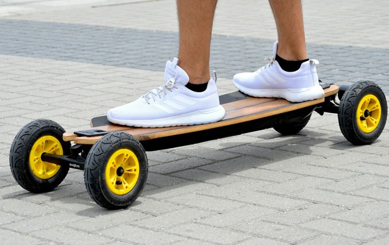 A person in white sneakers rides an electric skateboard