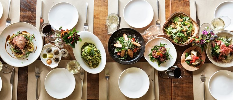 A large restaurant table filled with food and white plates.