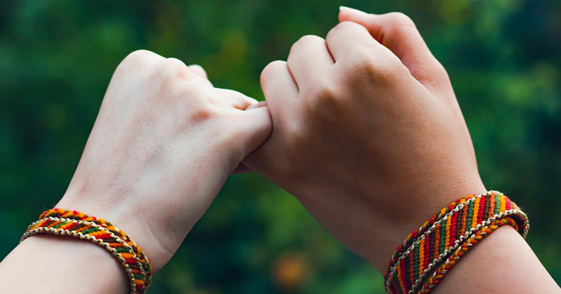 A pair of hands wearing friendship bracelets, linking together with their pinky fingers