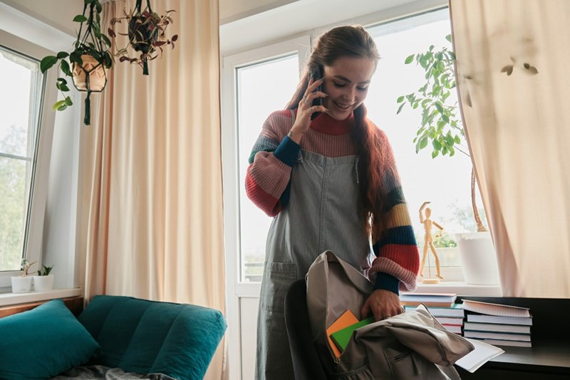 A young woman in a colorful sweater talks on the phone in her bedroom