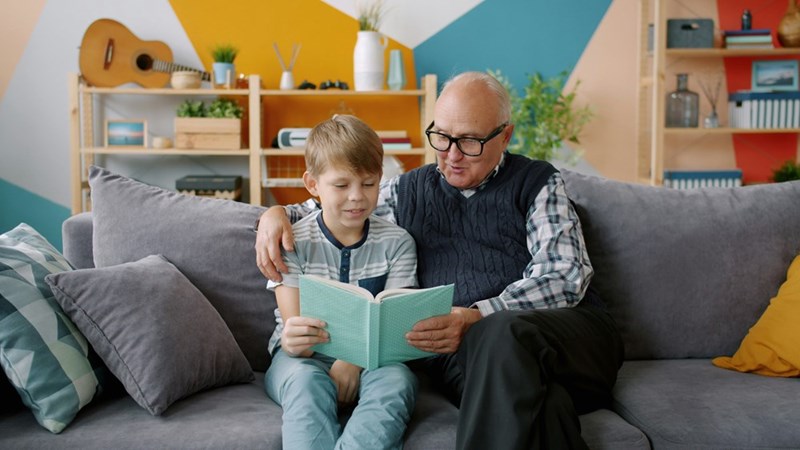 A grandad reading with his grandchild in a playroom.