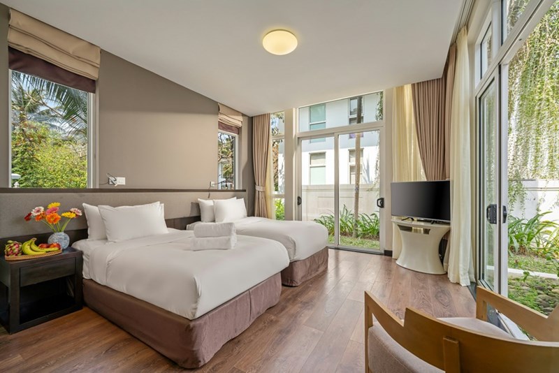Two neatly made beds inside a bright hotel room prepared for travelers sharing accommodation.