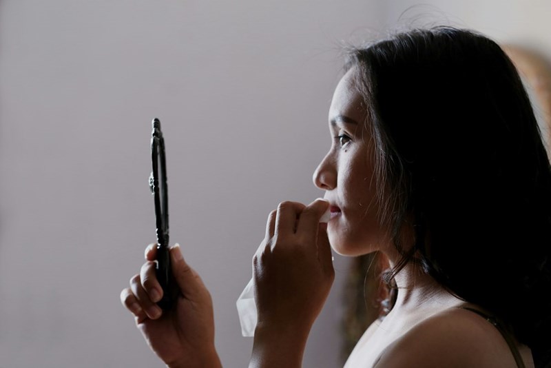 woman looking anxiously towards hand mirror
