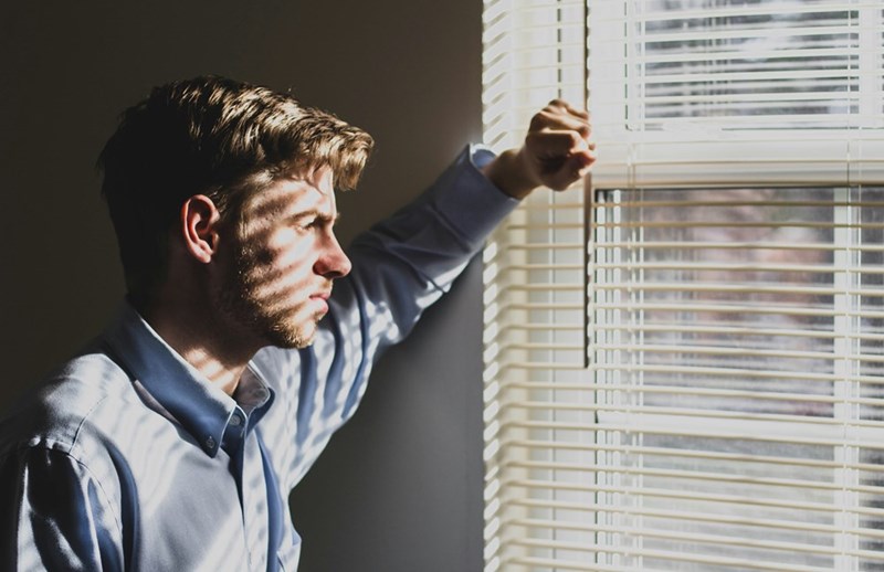 man looking through window with worried expression