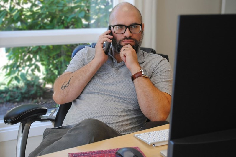 Man in glasses taking a phone call at a desk with a serious, focused look