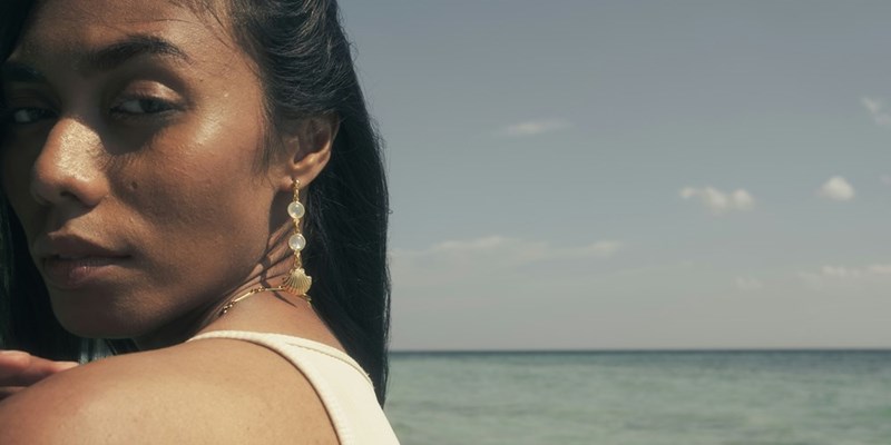 A woman looking at the camera, wearing jewelry and her hair down.
