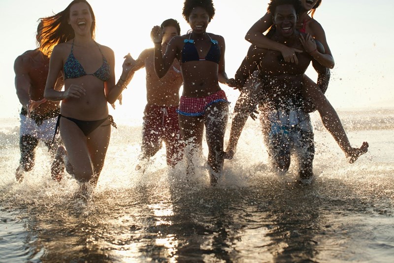 A group of friends running in the water at the beach and smiling.