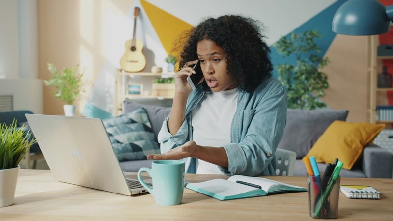 A woman talking on the phone while she uses her computer.