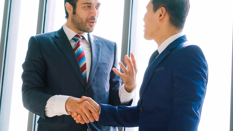 Two men wearing suits stretching hands making a deal.