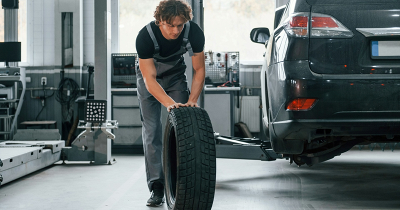 A young male mechanic rolls a tire across the shop floor
