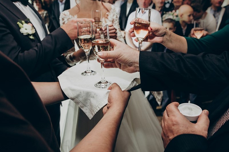 A bunch of hands hold champagne glasses toasting a couple at a wedding