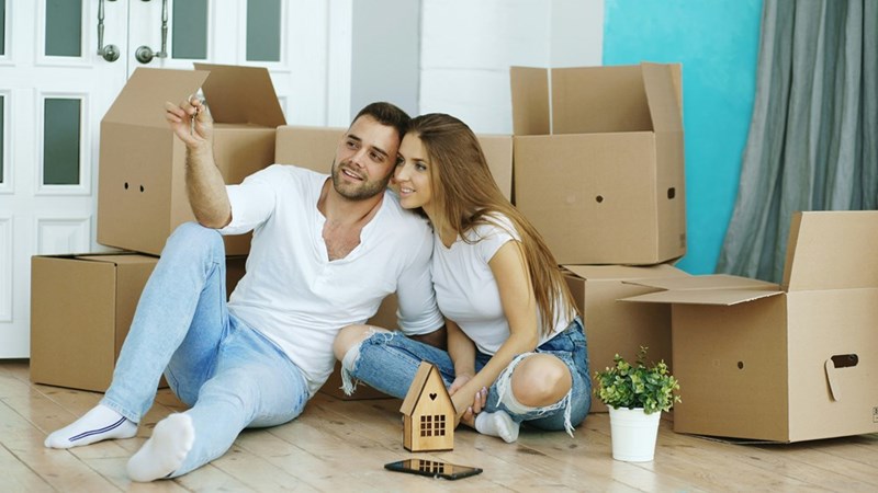 Young engaged couple sitting together among moving boxes after receiving the keys to their first home.