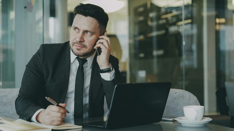 A stressed man at work sits at a desk and talks on the phone