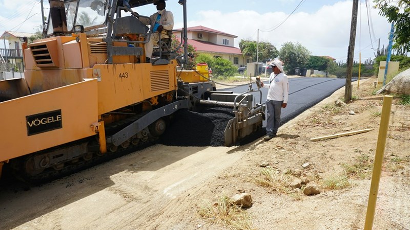 Heavy road-paving machine laying fresh asphalt during an unauthorized private-road construction project.