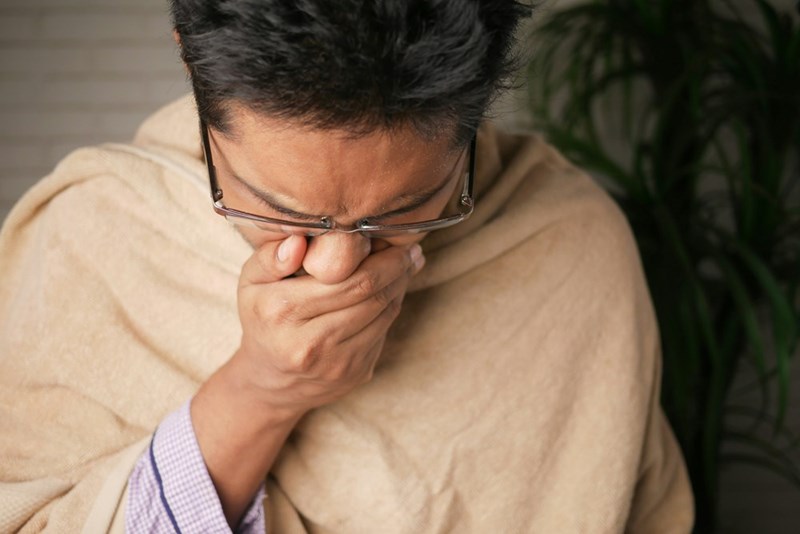 A man coughing onto his hand while being roped by a blanket. Representation.