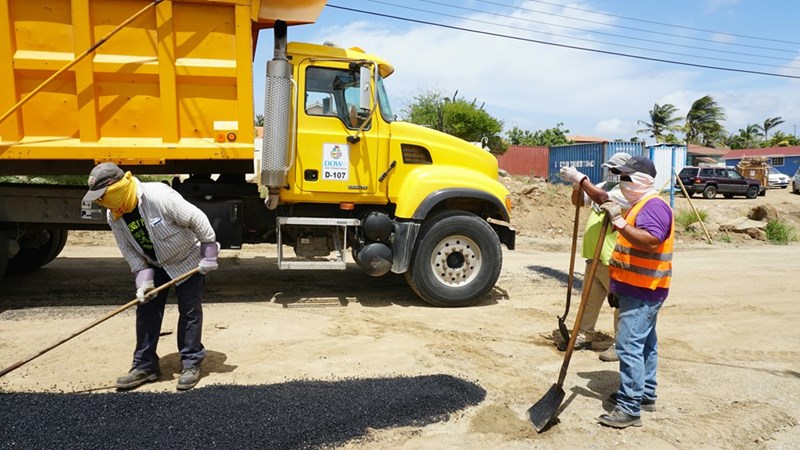 Construction crew and dump truck paving a road after a neighboring homeowner declined to fund the project.