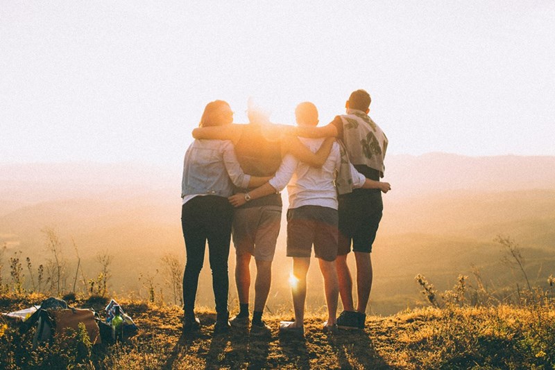 A group of four friends hugging and looking at the sunset. Representation.