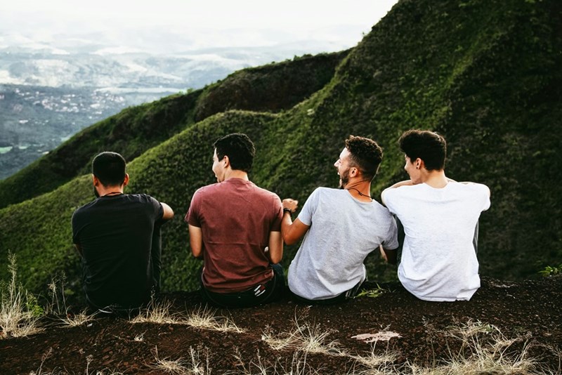 Four male friends laughing and talking at the top of a mountain. Representation.