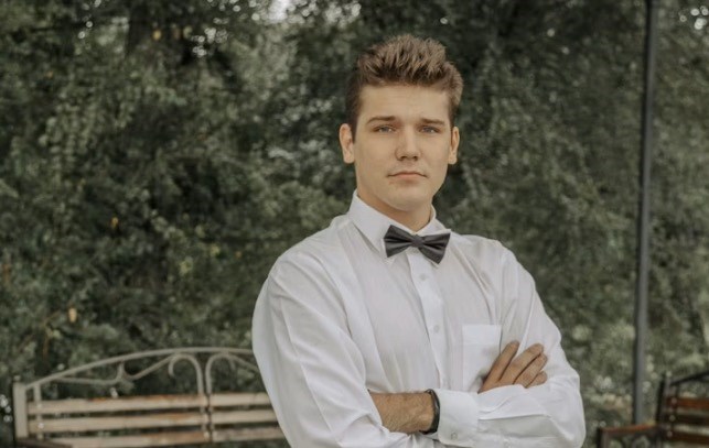 A waiter, nicely dressed, stands with his arms folded.