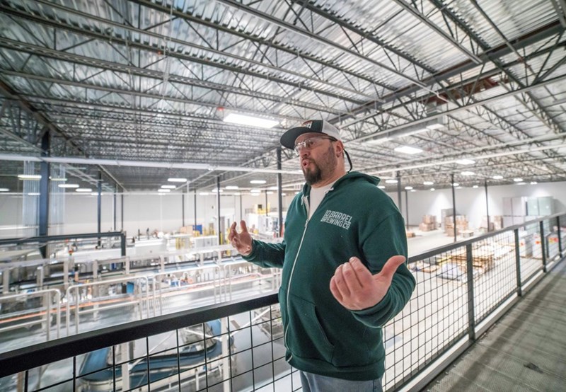 A warehouse worker stands near metal equipment explaining something