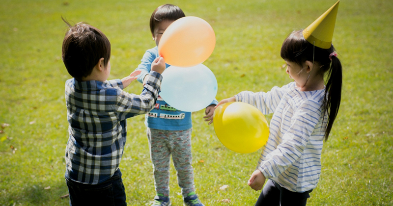 Three children standing in a circle on grass, playing with balloons