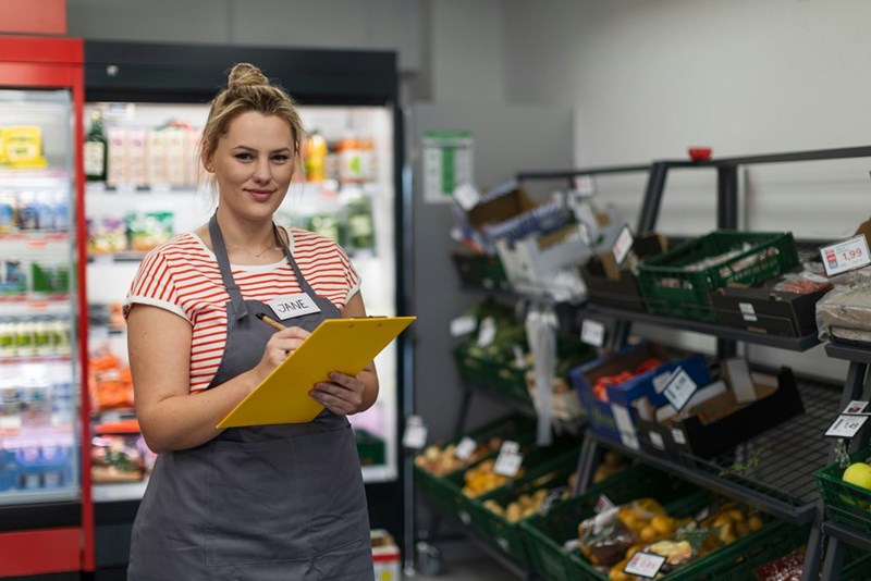 A supermarket manager takes notes on her clipboard.