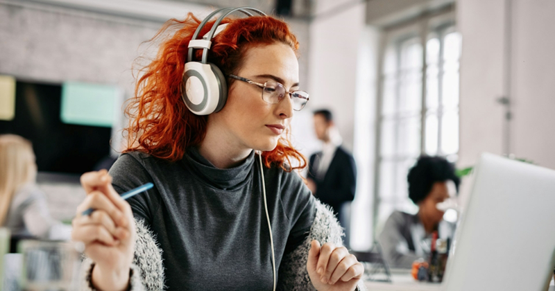 A representation of an employee listening to music on headphones while sitting in an open-plan office