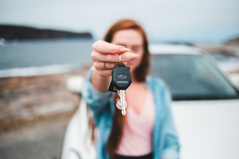 A young woman holding the car keys for the car behind her. Representation.