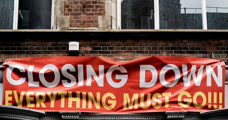 A red tarp sign attached to a building that says “closing down, everything must go”
