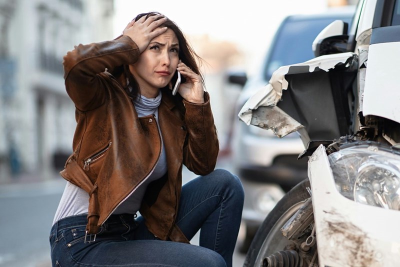 Driver making a phone call while inspecting serious front-end vehicle damage.