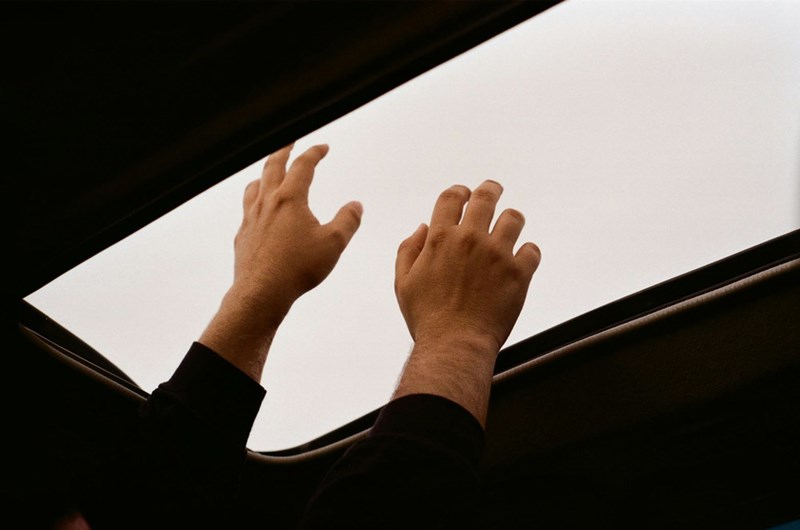 Teen reaching toward a car sunroof to open it.