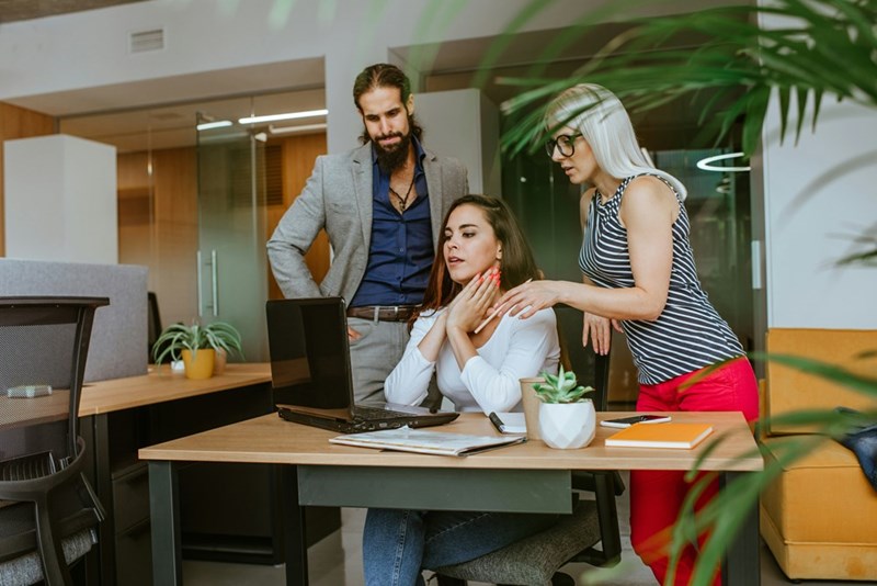 Senior engineer sitting at her desk while two managers explain an unexpected promotion she clearly doesn't want.