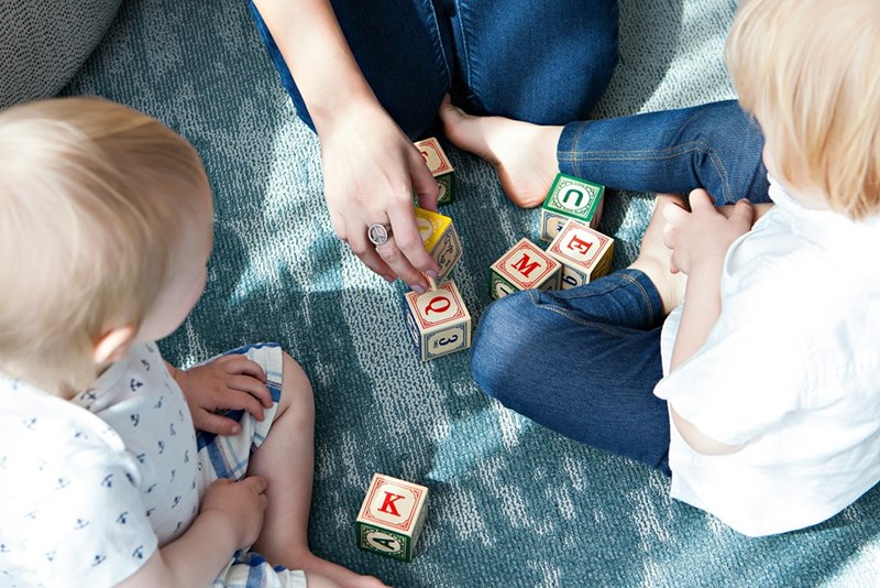 Two kids playing while an adult cares for them. Representation.