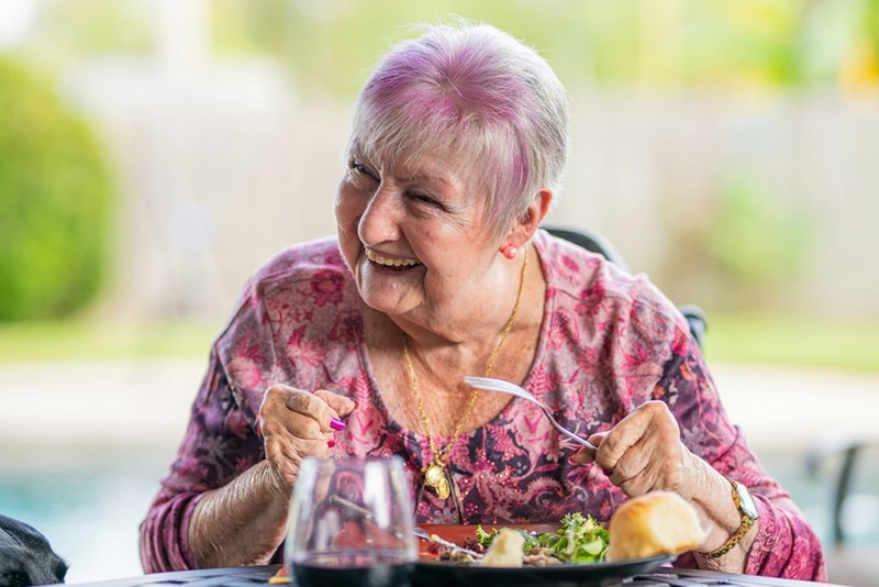 A happy grandmother sitting at a dining table during a family holiday, without knowing his daughter secretly hates her green beans.