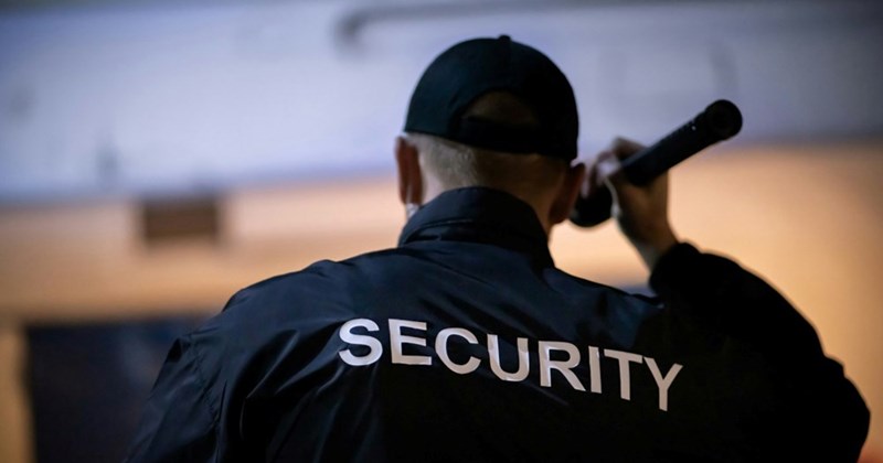 Close-up of the back of a security guard wearing a jacket that says ‘security’ shining a flashlight